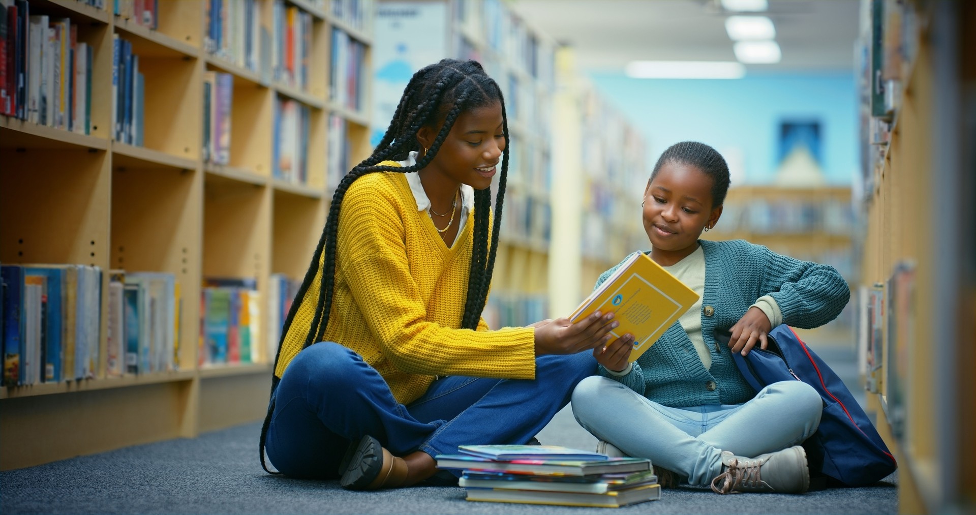 Library, child and teacher reading book for education, learning and knowledge for storytelling. Educator, black woman and girl on floor for fun, fantasy stories and language development or relaxing